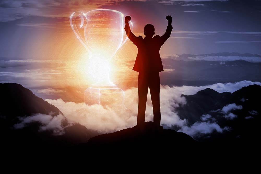 A picture of a man on a mountain top with hands raised